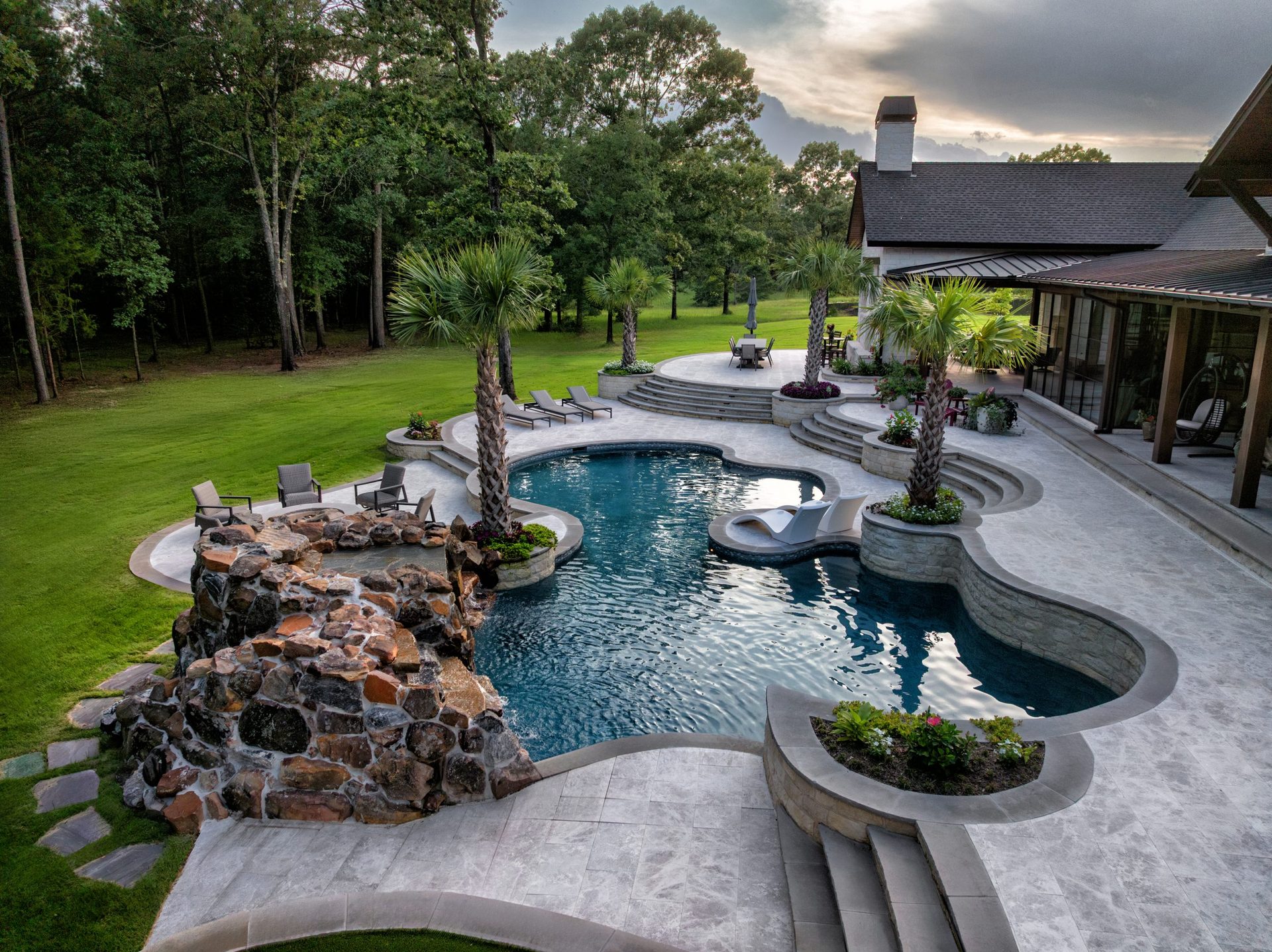 A remodeled freeform pool with a rock waterfall, palm landscaping, and a covered patio