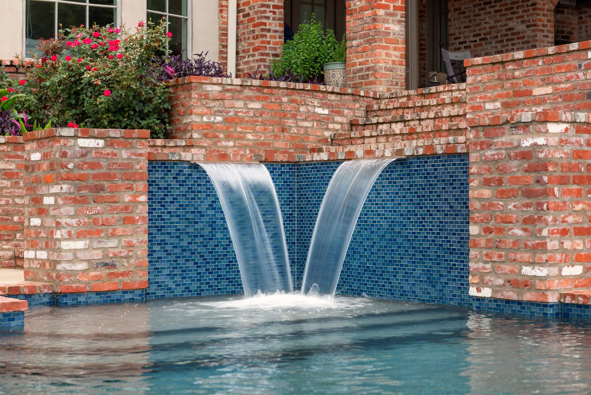Twin sheet waterfalls spilling over a glass tile wall into a remodeled pool